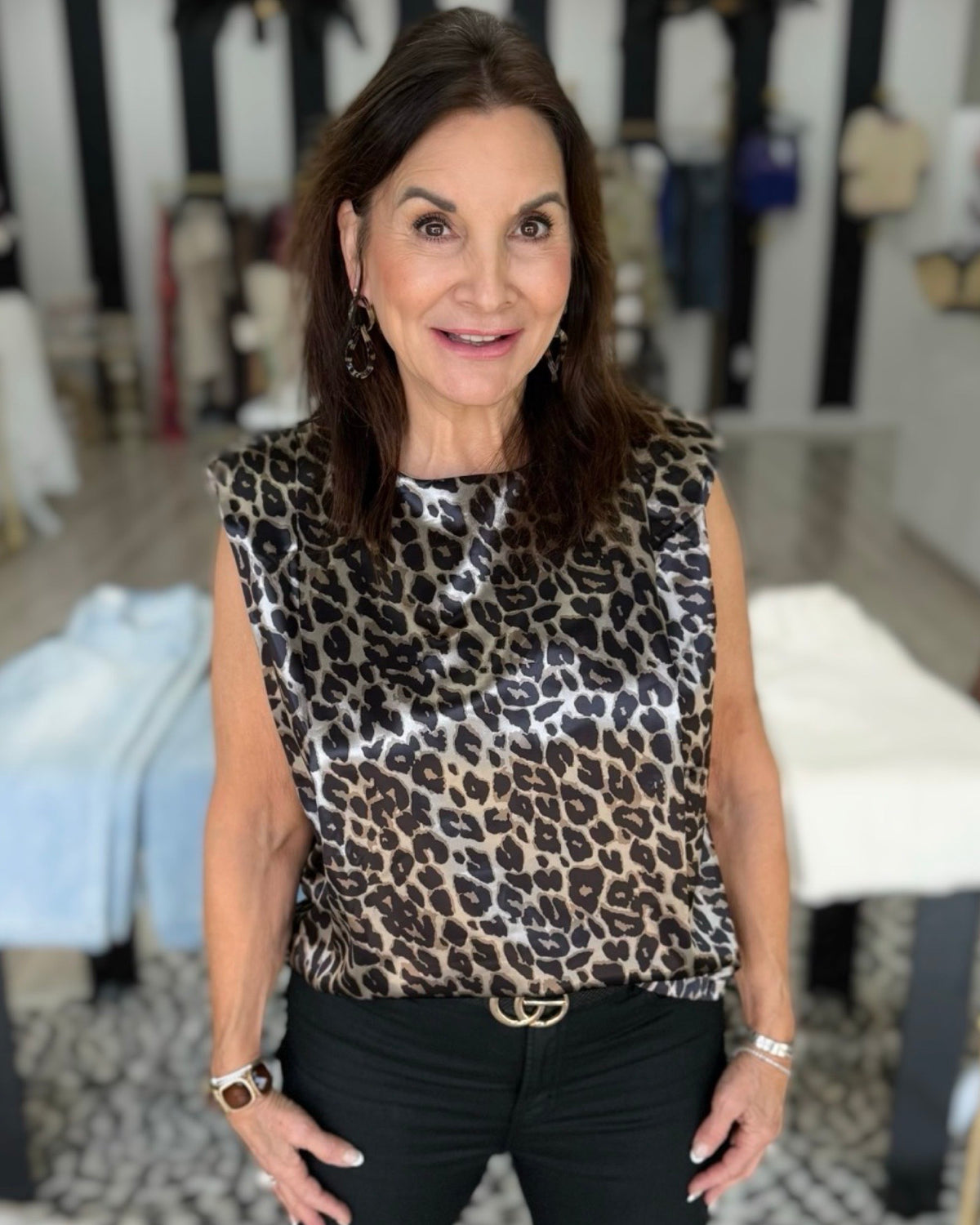 A woman wearing a sleeveless leopard-print top with black pants, standing in a boutique setting.