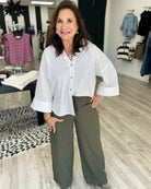 A woman modeling a white button-down shirt with three-quarter sleeves and olive green pinstripe wide-leg pants in a clothing boutique.