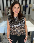 A woman wearing a sleeveless leopard-print top with black pants, standing in a boutique setting.