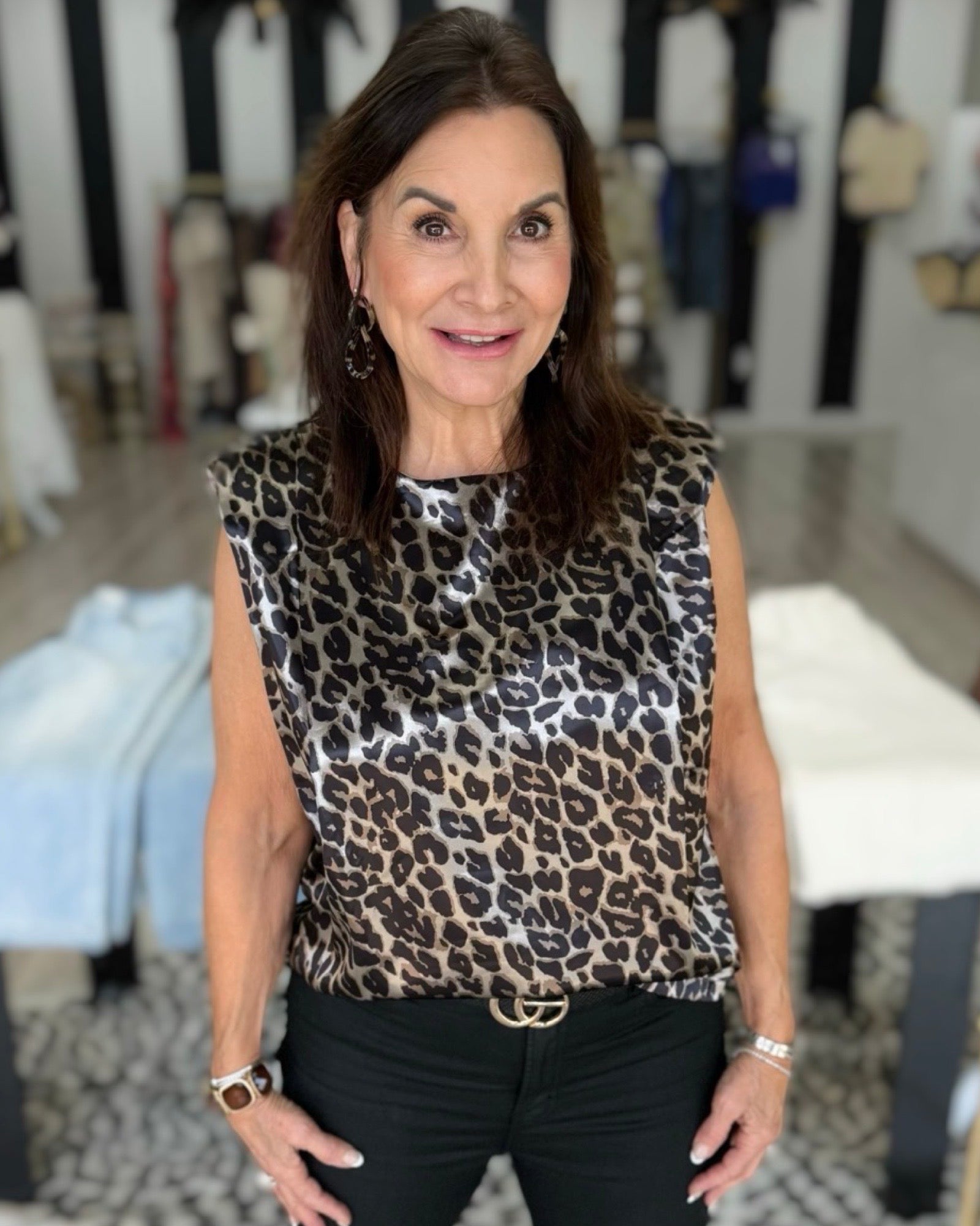 A woman wearing a sleeveless leopard-print top with black pants, standing in a boutique setting.