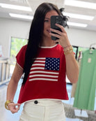 Person wearing a red shirt with an American flag design, taking a mirror selfie.